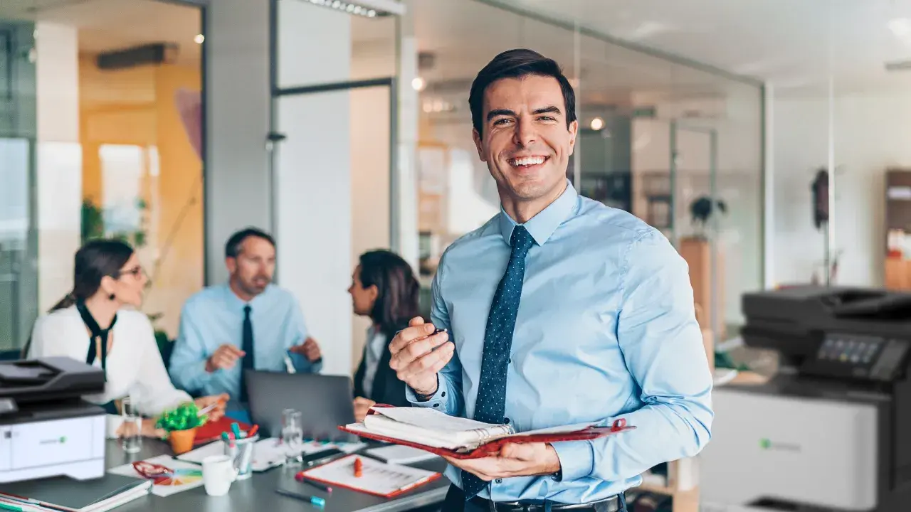 Imagen de un gerente feliz y celebrando porque tiene beneficios. De fondo o al rededor se muestran las impresoras y sus empleados trabajando felices.