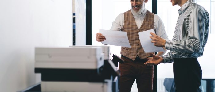 Cheerful colleagues discussing papers in office printer room